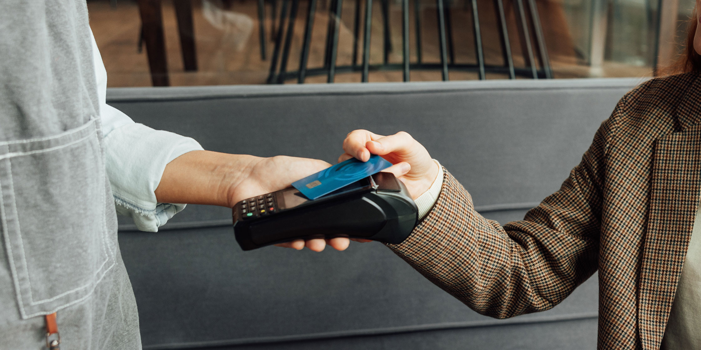 A merchant holds a card reader while a customer taps their card to pay.